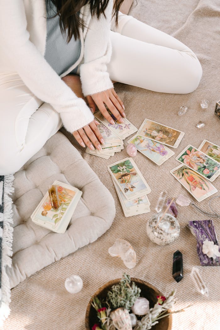 services-02 A woman sits cross-legged indoors, handling tarot cards, surrounded by crystals and herbs.